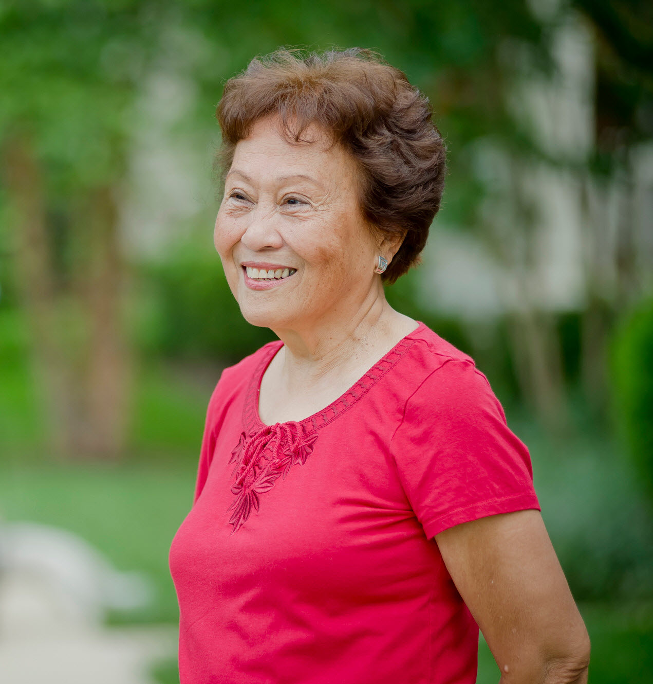 smiling Asian woman in red top stands on sidewalk