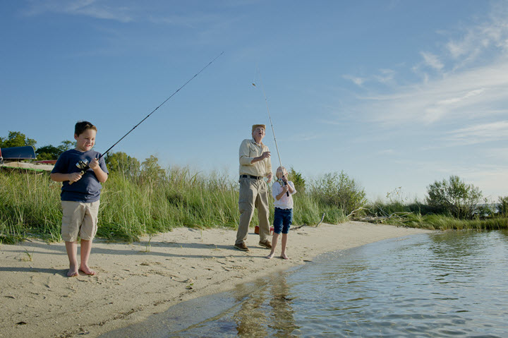 grandpa and his two grandkids in the sand barefoot, fishing into the water