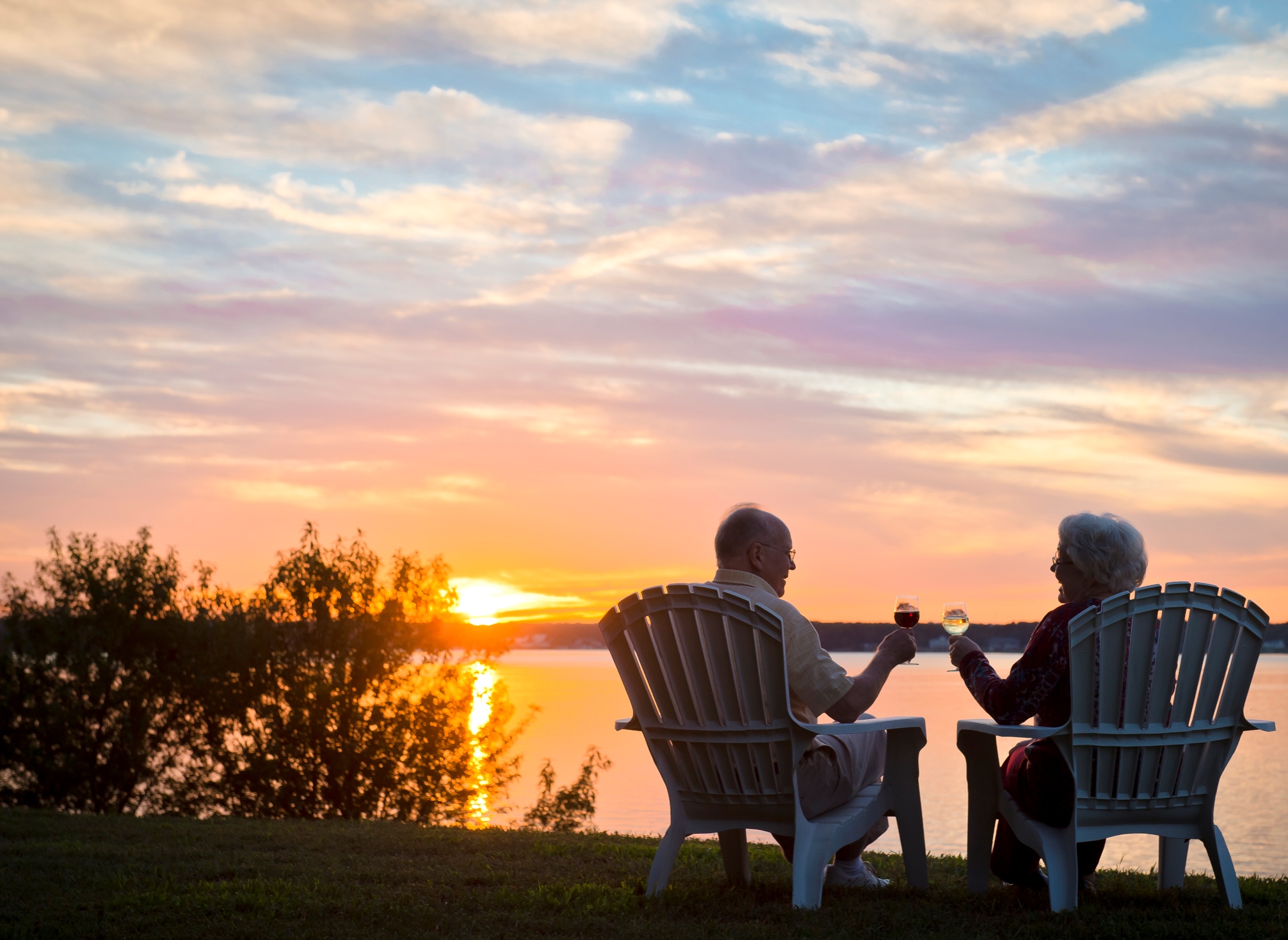 a couple in Adirondack chairs, sipping wine at sunset, waterfront