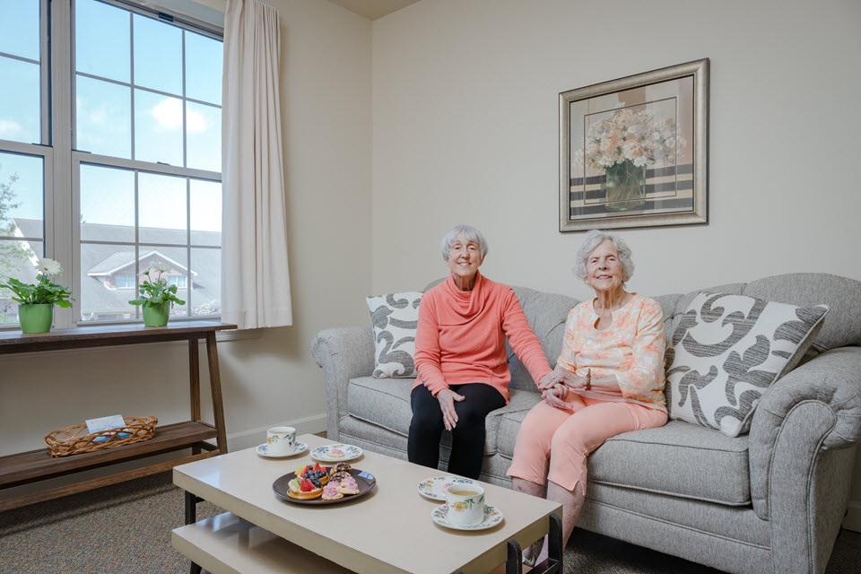 adult daughter sits with her mother in her assisted living apartment having tea