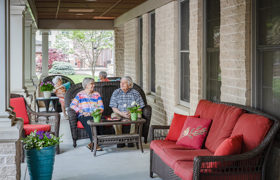 woman and man sit talking on the porch of bethany village assisted living building
