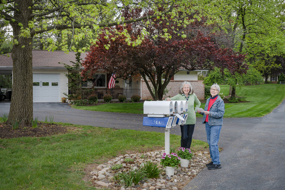 two senior women stand at end of cottage driveway getting the mail