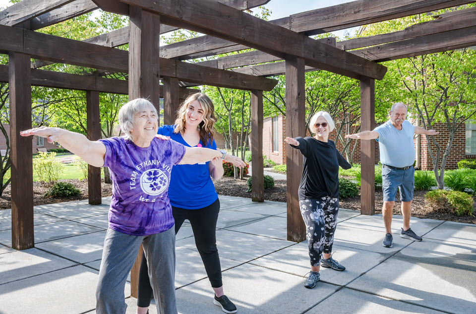 a fitness trainer helps position a senior woman during an outdoor yoga class