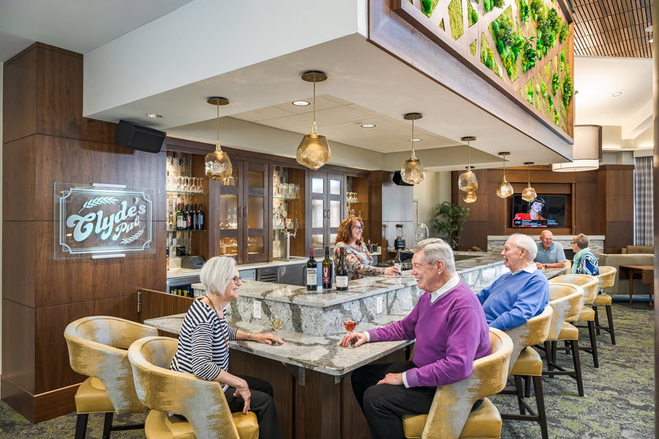 three people sit chatting in foreground of Clyde's pub at bethany village having wine and beer