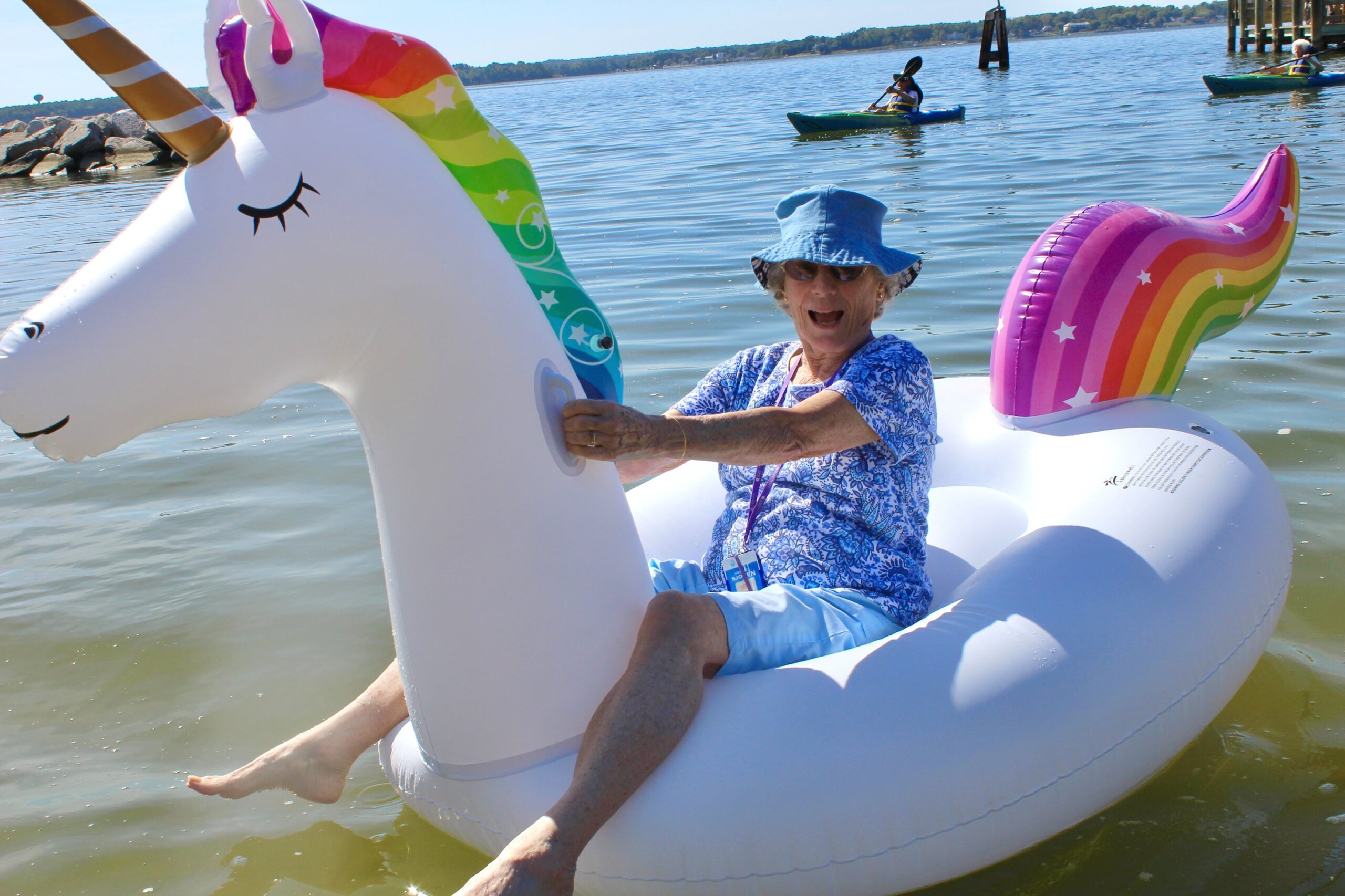 senior woman wearing bucket hat on a unicorn floatie in the water