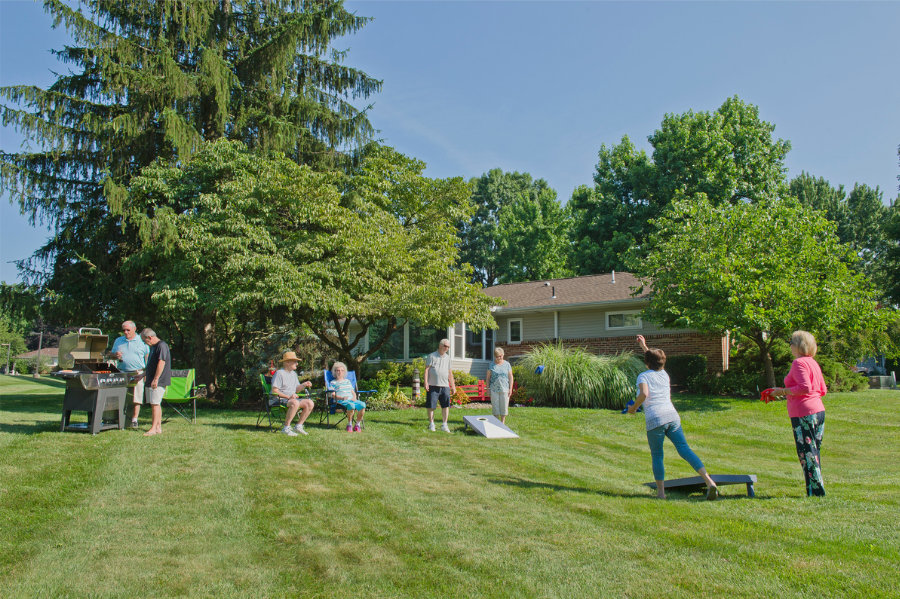 Eight senior adults at an outdoor backyard party grilling and playing corn hole