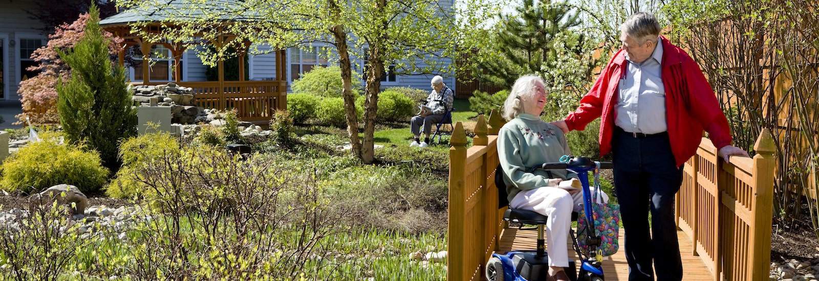 resident in electric wheelchair strolling with husband