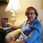 Springhill resident, Jean Dunn, in her Springhill apartment on her couch, holding a book.