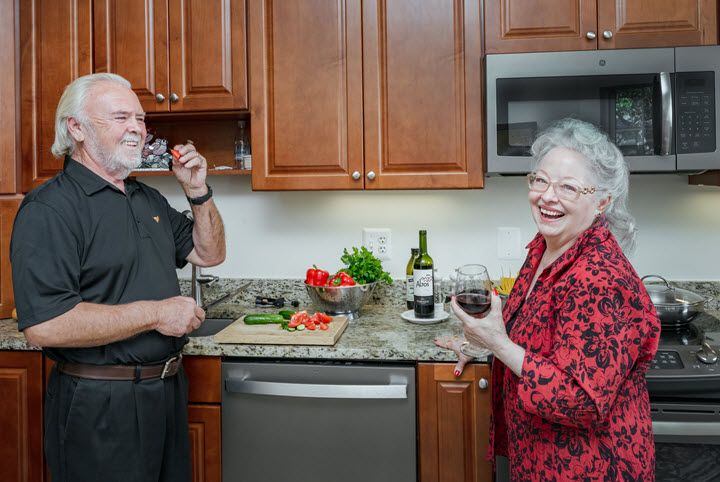 two seniors, a man and a woman, in a kitchen having wine and vegetables