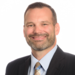 j.d. shuman headshot shows smiling white man in striped tie with stubble