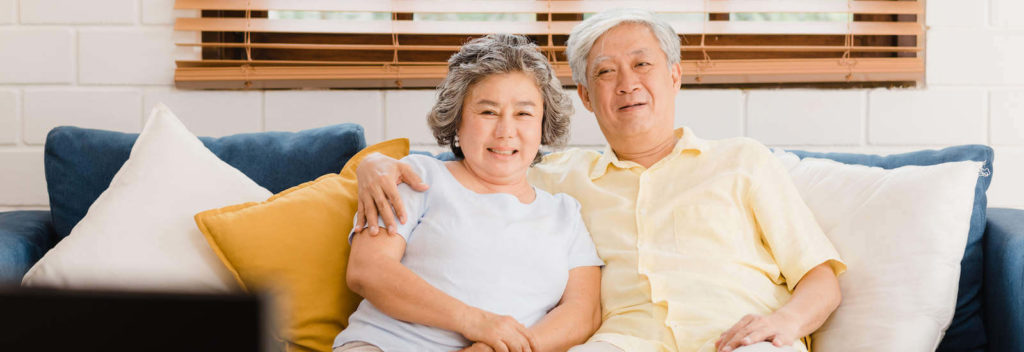 An Asian elderly couple smiling for the camera while sitting on a couch.