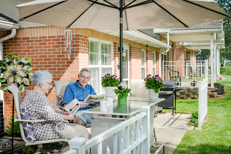 a man and woman sit on their back patio drinking coffee and reading paper
