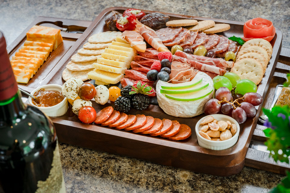 a beautiful charcuterie board with cheeses, wheel of brie, almonds, salami, and fresh berries