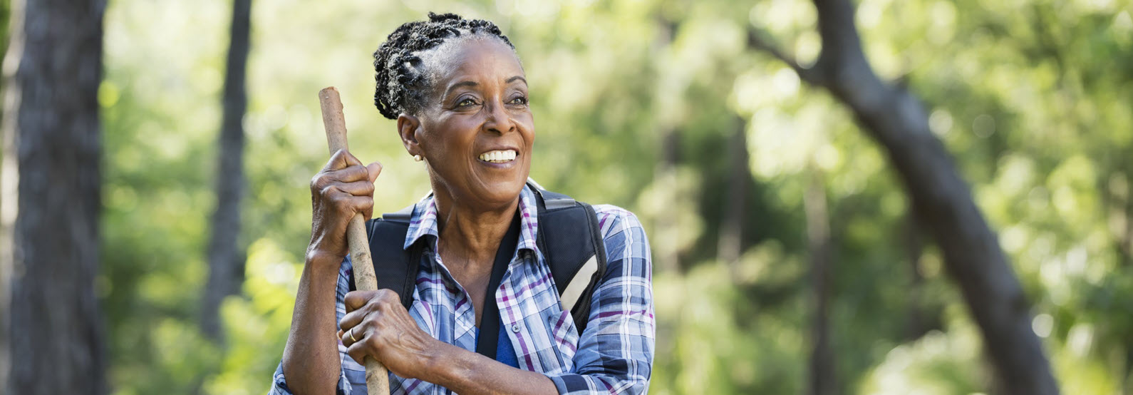 woman stands in woods with walking stick