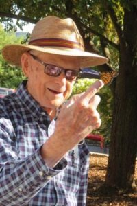 man standing outside in straw hat holding up finger with monarch butterfly on it