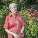 smiling senior woman standing in vegetable garden in front of tomato plants with garden clippers in her hands