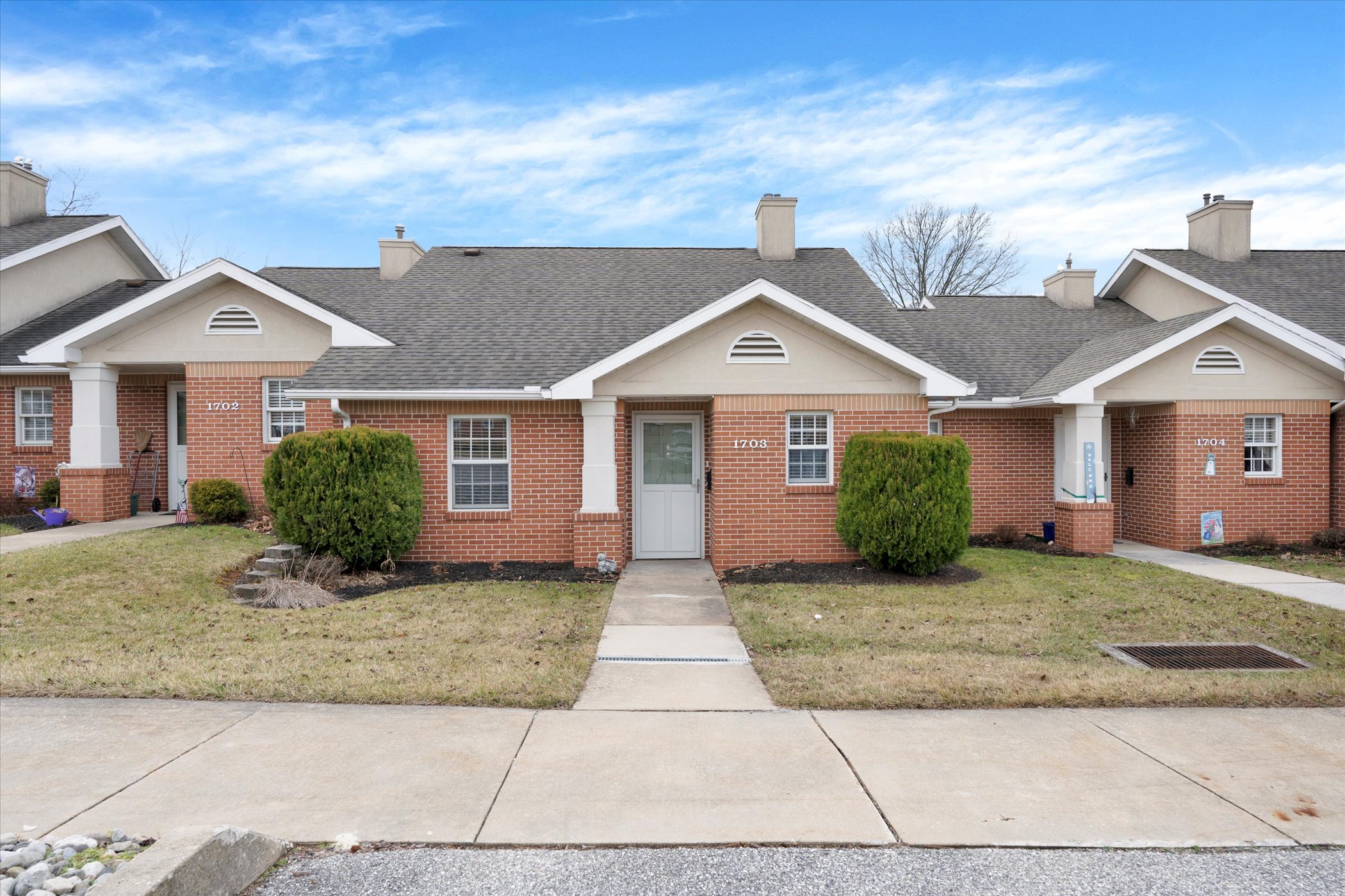 brick cottage with shrubs and white entry door and sidewalk leading to covered porch