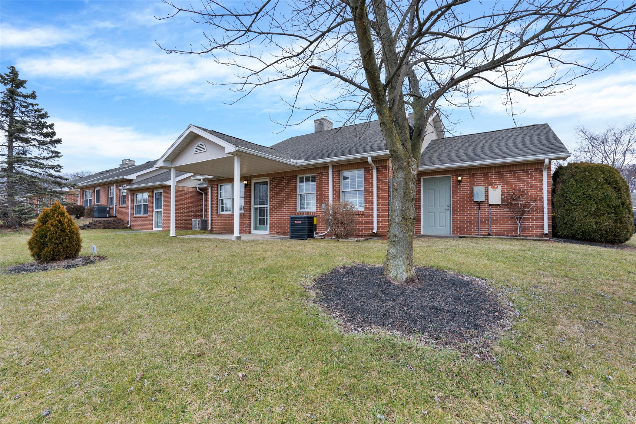 rear of brick cottage with covered patio and large lawn with tree