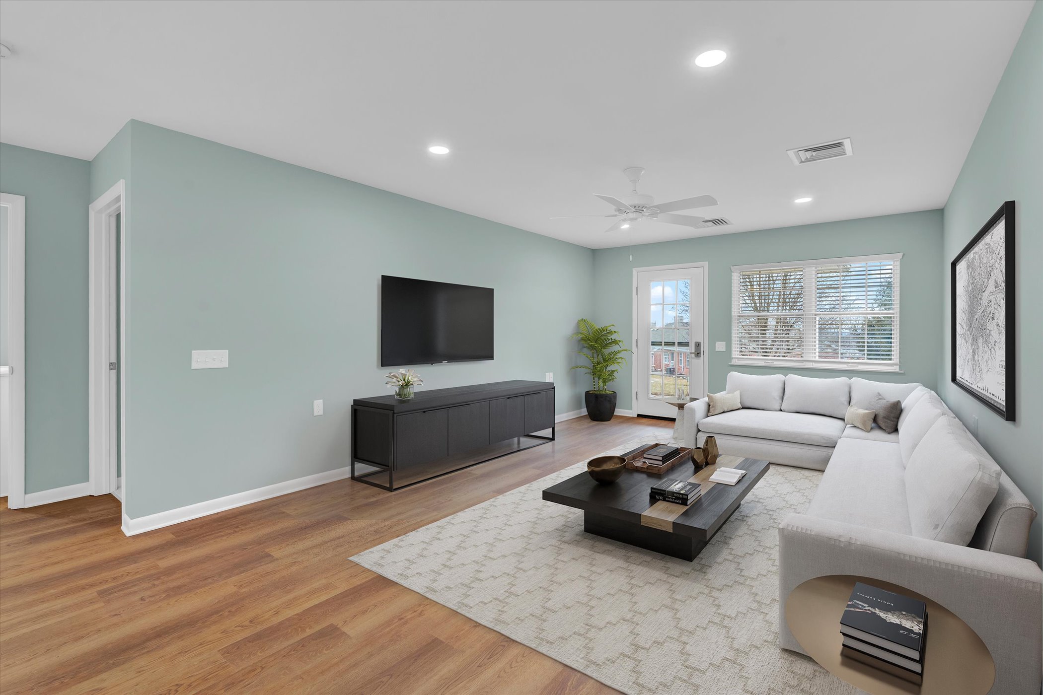 open floorplan living room with pale green walls, large window and french door, coffee table and sectional sofa with rug over hardwood floor