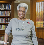 barbara harbison, a smiling african american senior female, leans against a table in a large library