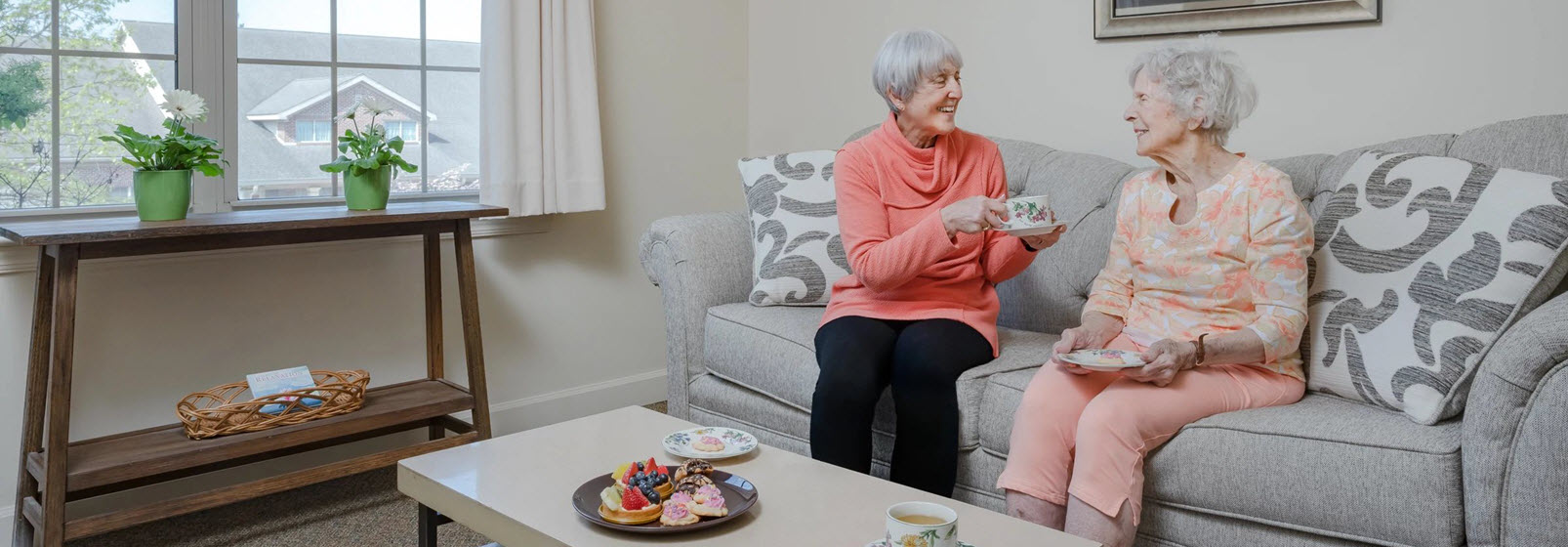 a mother and daughter sit on the sofa drinking tea and talking to each other