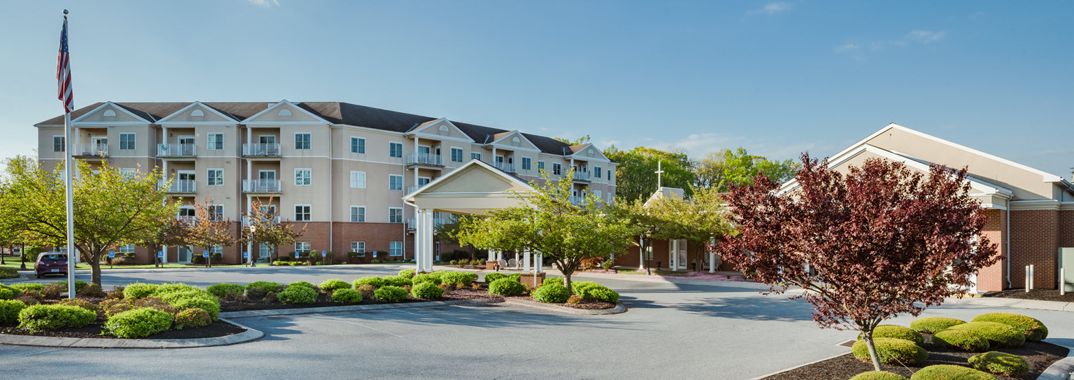 front of normandie ridge apartments with covered entrance, landscaped beds, and flag