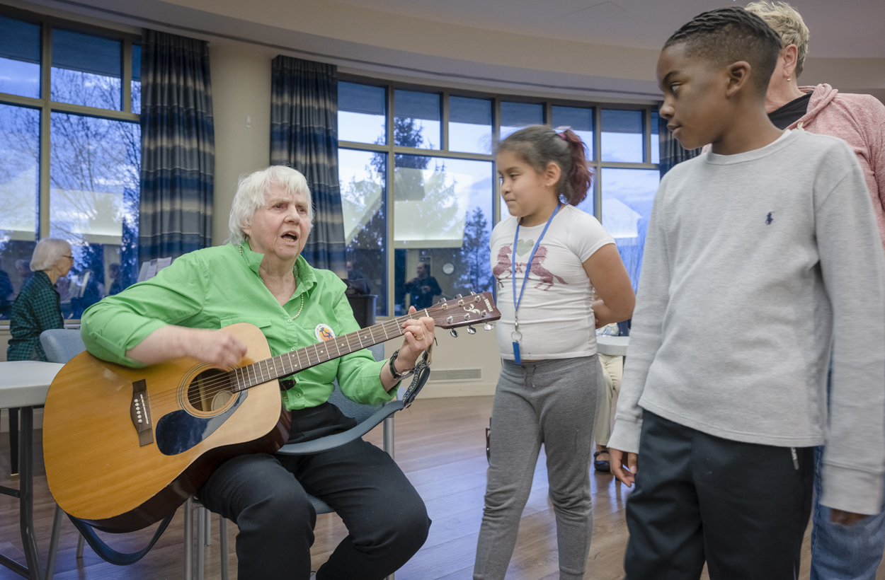 senior woman white hair playing guitar for two young children