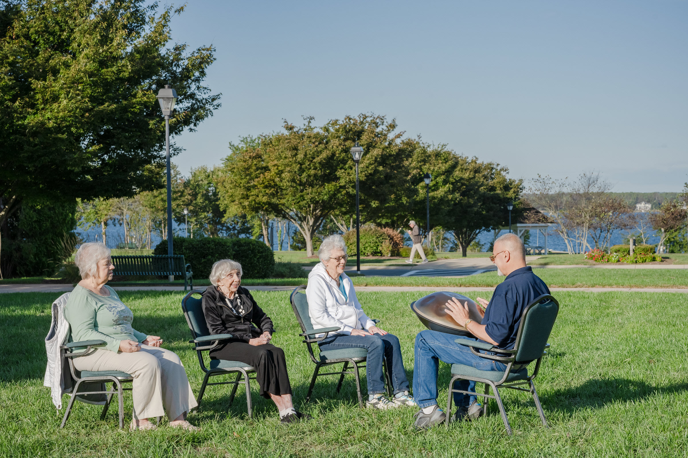 four seniors sitting in chairs outside, one of them playing an instrument