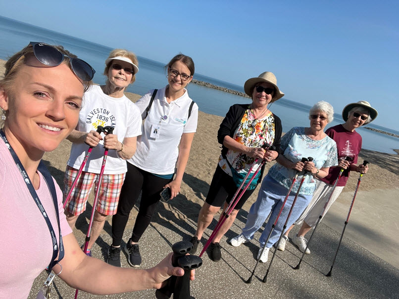 Springhill wellness employee and five senior woman stand on shore of lake erie while on urban poling walk