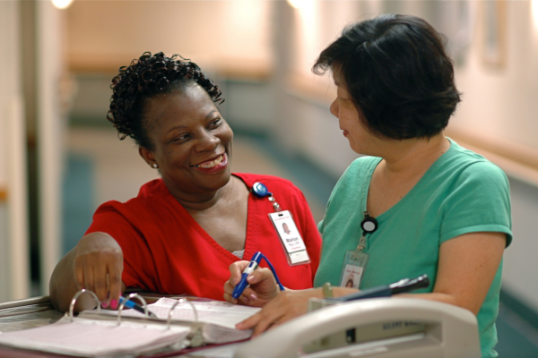 two nurses one black one asian talking over paperwork in hospital