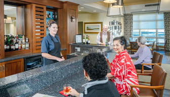 two senior women at TopSide Pub talking to each other with bar tender serving a glass of wine