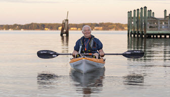 senior man floats in kayak on patuxent river with sun setting