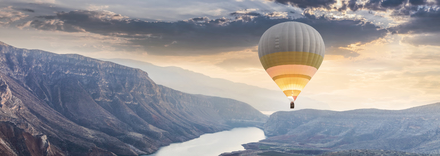 hot air balloon at sunrise floats above a vast canyon with river flowing through it