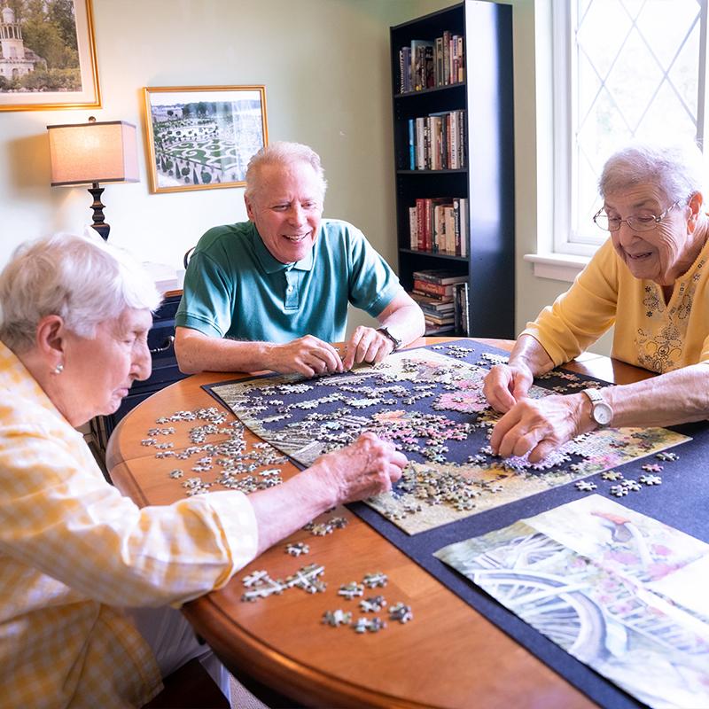 group of three seniors, one man and two women doing a puzzle together