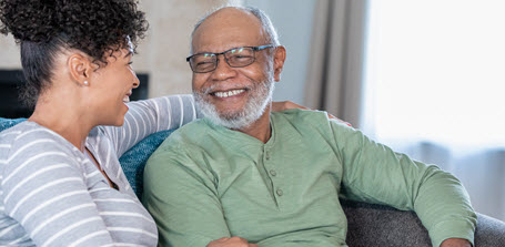 smiling senior African American man sits on couch with his daughter