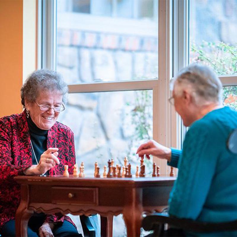 two older women playing chess together in a common room