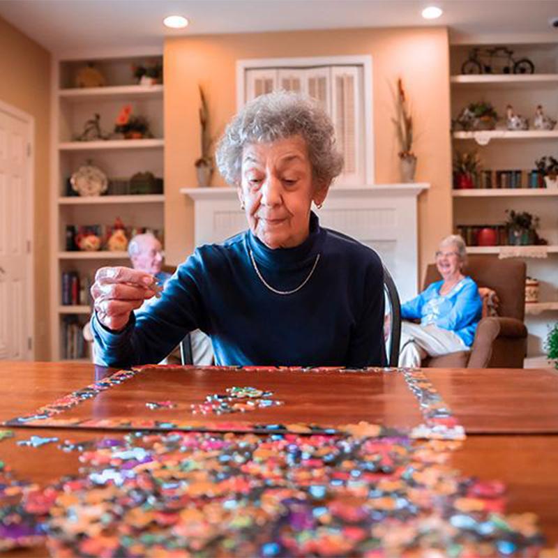 older woman sitting in common area doing a puzzle with two residents behind her