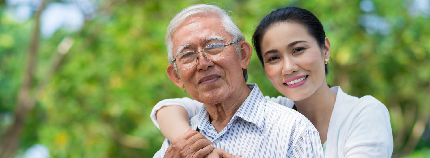 smiling, white-haired asian man stands outside with his adult daughter