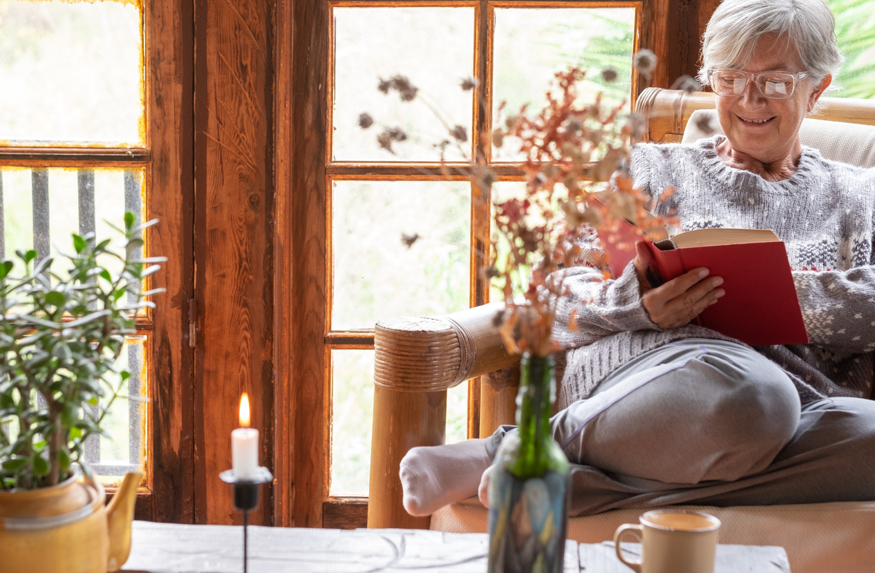 Attractive relaxed senior woman sitting at home in an armchair reading a book. Elderly smiling caucasian woman enjoying reading pleasure in retirement
